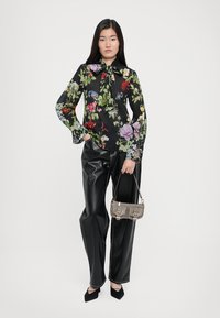 Floral blouse with black background, long sleeves, and tie collar. Paired with high-waisted black leather trousers and a small gray handbag.