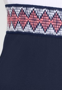 Marine stof met een decoratieve tailleband versierd met witte, koraalrode en marineblauwe geborduurde geometrische patronen. Over het algemeen een gladde textuur.