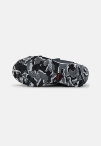 Black and gray athletic shoe sole with rugged traction pattern, featuring a mix of solid and splattered designs, and a red branding accent.