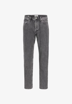 Personne portant un t-shirt blanc uni à manches courtes, un jean ample gris délavé à l'acide et des baskets blanches avec des détails noirs, debout devant un fond uni.