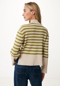 Cardigan en tricot rayé crème et vert olive, avec une texture côtelée et des coutures d'épaule tombantes. Porté sur un jean bleu foncé.