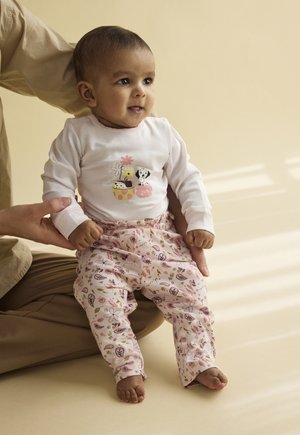 Body bianco a maniche lunghe con grafiche colorate di cartoni animati, abbinato a pantaloni rosa con disegni floreali e paisley.
