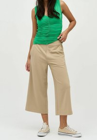 Zelený řasený top, béžové široké kalhoty a béžové tenisky. Materiál je hladký s mírným leskem a střih je volný.