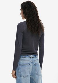 Dlhý rukáv tmavosivého trička s priliehavým strihom, skombinovaný s voľnými svetlomodrými riflovými šortkami s veľkými zadnými vreckami.