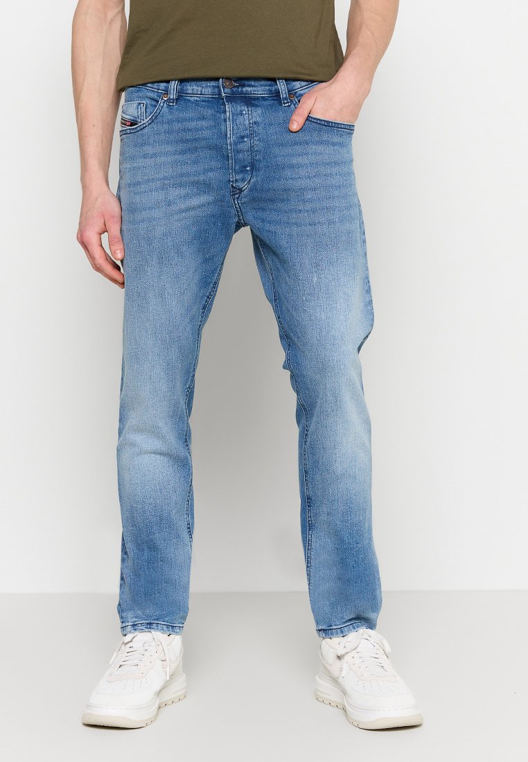 Jean en denim bleu clair avec une coupe droite, présentant cinq poches et une texture légèrement délavée. Associé à des baskets blanches.