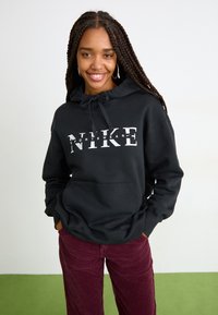 Crna dukserica s kapuljačom, s bijelim ispisanim „NIKE“ logotipom i „SPORTSWEAR“. Uparena s bordo akom.