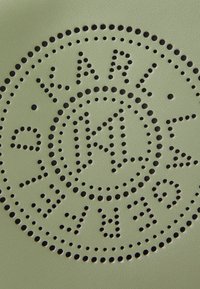 Zeleni kožni materijal s kružnim uzorkom i perforiranim crnim uzorcima, uključujući stilizirani logo u središtu.
