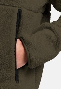 Fleece jacket in olive green with a textured, soft finish; features a black zippered pocket and a fitted cuff design.