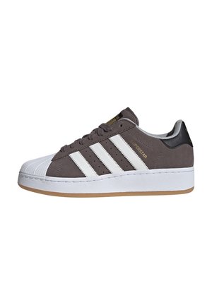Lage grijze sneaker met witte rubberen neuskap, witte strepen aan de zijkanten, dikke witte zool en een zwarte hieltab.