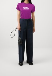 Camiseta de manga corta morada con el logotipo "KARL LAGERFELD" combinada con pantalones de pierna ancha de tiro alto en azul marino y un pequeño bolso negro.