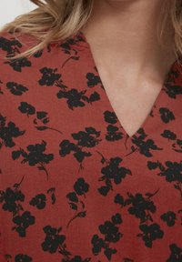 Tissu à motifs floraux rouges avec des fleurs noires, présentant un design en v et une texture lisse. Gros plan sur l'encolure et les détails du motif.