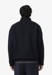 Giacca blu navy in misto lana con colletto alto, spalle scese e orlo a coste. Tessuto morbido con una vestibilità leggermente oversize.