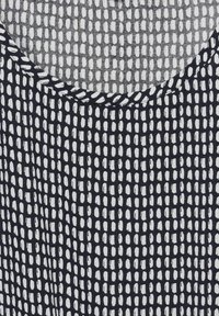 Tessuto a righe bianche e nere con grafiche ovali, trama testurizzata e scollatura rotonda. Il design ha un aspetto moderno e geometrico.