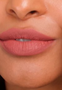 Gros plan sur des lèvres avec un rouge à lèvres mat rose et une bouche légèrement entrouverte, montrant une texture de peau lisse autour des lèvres et du menton.