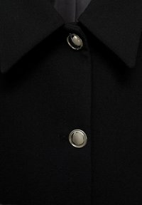 Palton din țesătură neagră, cu o guler mare și închidere cu nasturi de nuanță argintie. Textura este netedă, având un design clasic și minimalist.