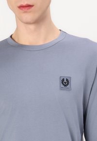 Világoskék, hosszú ujjú, puha anyagból készült ing, kerek nyakkivágással és fekete logóval a bal melle részen.