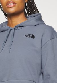 Felpa blu chiaro con cappuccio regolabile. Presenta un logo ricamato nero sul lato sinistro del petto. Tessuto morbido con orlo e polsini a costine.