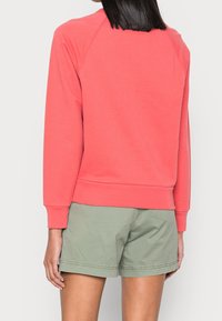 Felpa color corallo con maniche a raglan, finitura testurizzata e orlo a coste; abbinata a pantaloncini verde chiaro, con una vestibilità rilassata.