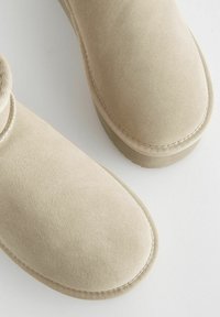 Bottines en daim beige avec une texture douce, un bout arrondi et des détails cousus. Design profil bas avec une semelle plate pour le confort.