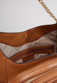 Intérieur d'un sac à main en cuir marron avec une poche zippée et une doublure en tissu lisse à motif en losanges. Détails en métal doré visibles.