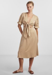 Abito di raso beige con scollatura a V profonda, maniche puff corte e cintura annodata. Tessuto liscio, di lunghezza media, con una vestibilità comoda.