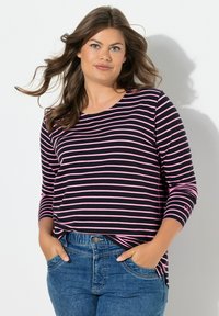 Černý a růžový pruhovaný top s dlouhým rukávem a kulatým výstřihem, z měkké bavlněné látky, volného střihu a s bočními rozparky, doplněný modrými džínami.