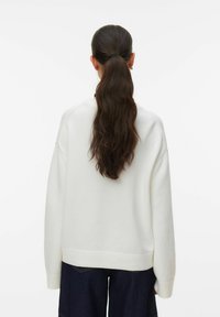Pull en tissu tricoté blanc, à coupe décontractée, avec poignets et ourlet côtelés, présentant une coupe à épaules tombantes et une finition texturée.