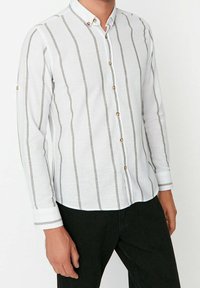 Valkoinen pitkähihainen paita, jossa harmaat pystysuorat raidat. Mukana napillinen kaulus ja koristeelliset kultaiset napit. Kuvioitu kangas.