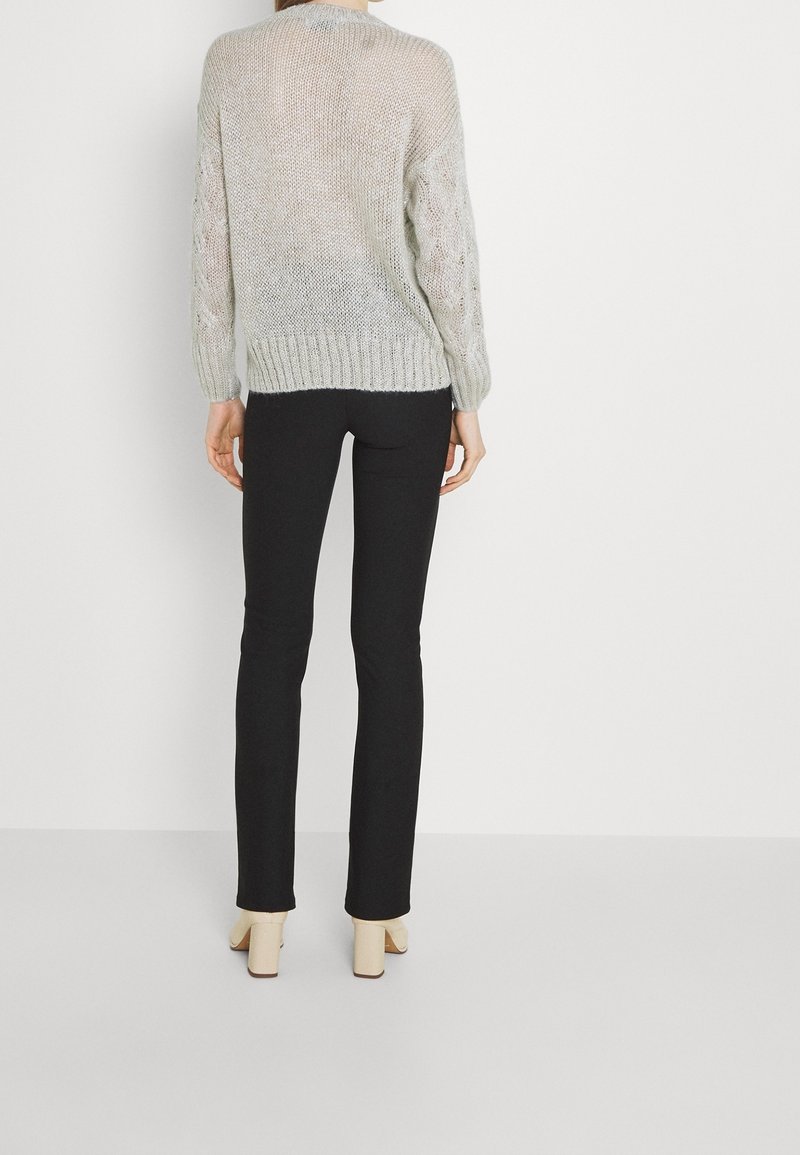 Pull en tricot gris clair avec un motif ajouré, ourlet côtelé et manches longues, associé à un pantalon noir ajusté et des chaussures à talons carrés beiges.