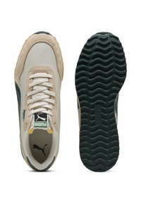 Puma-sneakers med en beige overdel og grønne accenter, teksturert semsket skinn og en bølgete gummisåle. Snørebåndene er hvite; logo på tungen.