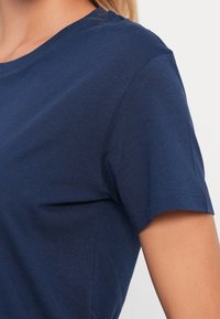 Tumehall sinine puuvillane T-särk ümmarguse kaelusega ja lühikeste varrukatega. Omab sileda tekstuuri ja lihtsat disaini.