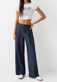 Vitt, kort, texturerat topp med blå text; vida, marinrandiga byxor med slät tyg; parat med vita sneakers.