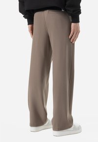 Pantalons larges à coupe décontractée en tissu beige doux, présentant une texture lisse, une poche arrière, et associés à des baskets blanches.