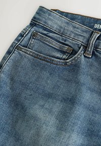 Modré džínsy z denimu s vyblednutým umývaním, s medeným šitím, klasickým dizajnom s piatimi vreckami a kovovými nitmi na predných vreckách.