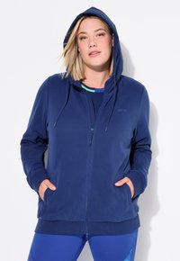 Felpa con zip blu navale, cappuccio con cordino, due tasche frontali, polsini e orlo a costine, realizzata in stoffa morbida. Presenta un logo discreto sulla parte frontale.