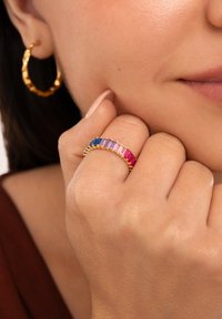 Guldtonad bandring med rektangulära färgade stenar i blått, rosa och lila. Texturerade hoops i guld som bärs i örat.