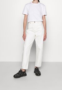 Biała bawełniana koszulka z krótkim rękawem, w zestawie z wysokimi białymi spodniami dżinsowymi. Czarne sportowe buty z teksturowanymi akcentami dopełniają stylizację.