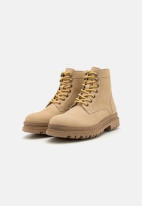 Bottines en cuir tan avec une finition texturée, bout rond, lacets jaunes et semelle en caoutchouc robuste avec des profondeurs pour une meilleure adhérence.