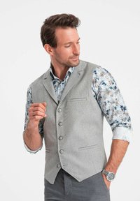Gray textured vest with five buttons, worn over a floral-patterned shirt. The outfit features a tailored fit and contrasting colors.