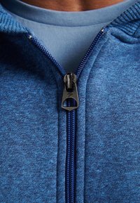 Felpa blu con zip, caratterizzata da una superficie texturizzata, con un design monocolore e una zip argentata con un tirazip.
