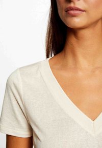 T-shirt crema con scollo a V e maniche corte, realizzato in tessuto morbido, caratterizzato da una texture sottile e una silhouette rilassata e aderente.