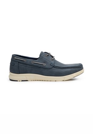 Zapatos de barco de gamuza azul marino con suela blanca, que cuentan con ojales y cordones plateados, textura suave y un diseño de punta rectangular.