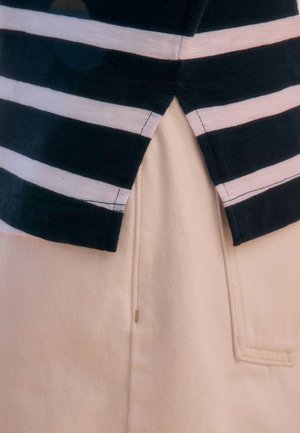 Marineblaue und weiß gestreifte Stoffoberteil mit geteiltem Saum, überlagert von einem hellbeigen Baumwollmischgewebe-Unterteil mit einer Taschenapplikation.