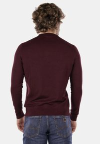 Maglione bordeaux realizzato in tessuto a maglia morbida con colletto rotondo e maniche lunghe, abbinato a jeans denim blu con tasche posteriori.