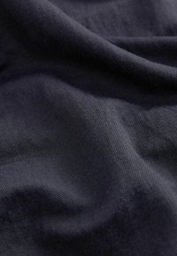 Sötét tengerészkék anyag, sima, puha textúrával, finom redőkkel és hajlításokkal, amely bemutatja az anyag súlyát és folyékonyságát.