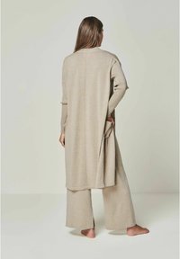Langer beiger Cardigan mit lockerer Passform, aus weichem Stoff, mit Seitentaschen und geradem Saum, kombiniert mit passenden weit geschnittenen Hosen.