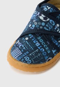 Blauwe canvas schoen met een patroon van sportgerelateerde tekst en iconen. Rubberen zool met een ronde neus. Elastische banden voor gemakkelijk aantrekken.