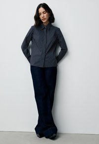 Donkerblauw gestreept overhemd met een puntige kraag en een voorste knoopsluiting, gecombineerd met donkerblauwe wijde spijkerbroek en zwarte schoenen met hak.