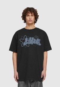 Crna oversized majica s plavim grafičkim printom koji sadrži tekst "Izgubljena mladost" uz motive cvijeća i zvjezdica. Pamuk, kratki rukavi.