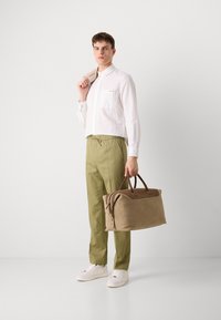 Camicia bianca con taschino sul petto, chinos verde oliva e borsa a tracolla marrone. Tessuto texturizzato e accenti marroni in contrasto.
